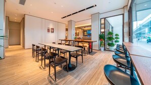 A modern dining area with a long table, multiple chairs, and a kitchen visible in the background.