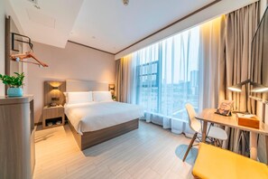 A modern hotel room with a large bed, a desk with a chair, a small table with a lamp, and a view of the city through large windows. - Hanting Hotel (Chongqing)