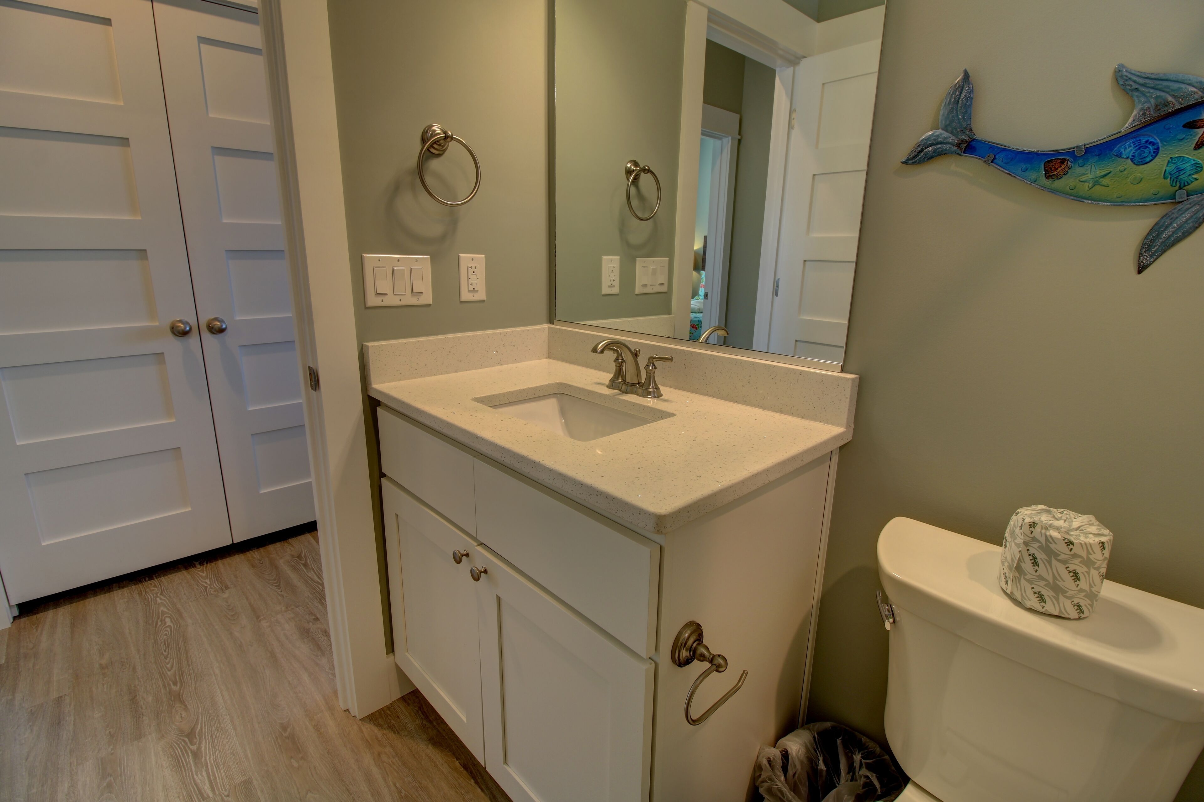 A bathroom with a white vanity, a large mirror, a toilet, and a wall-mounted fish decoration.
