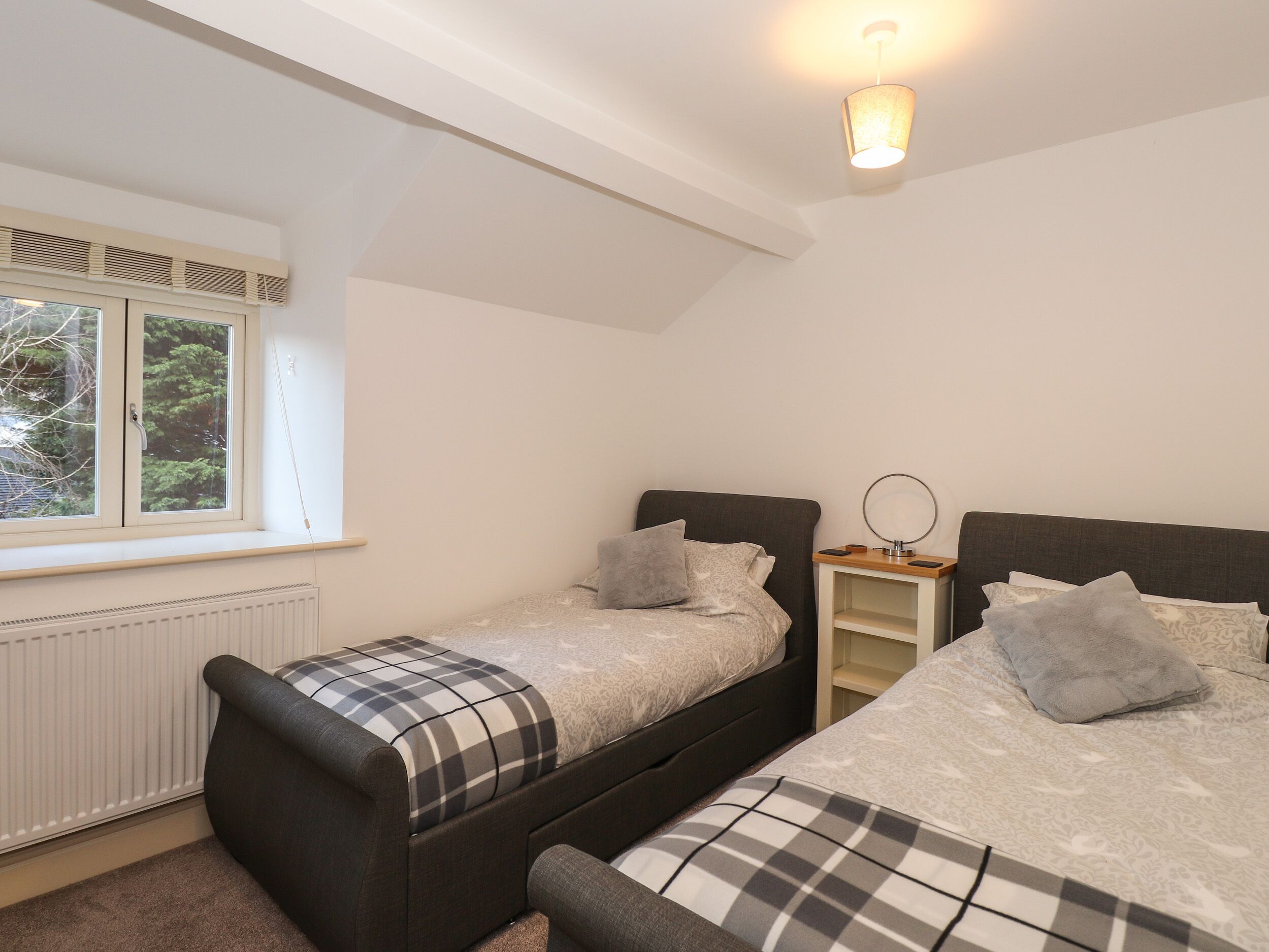 A bedroom with two beds, a window with blinds, a radiator, and a ceiling light.