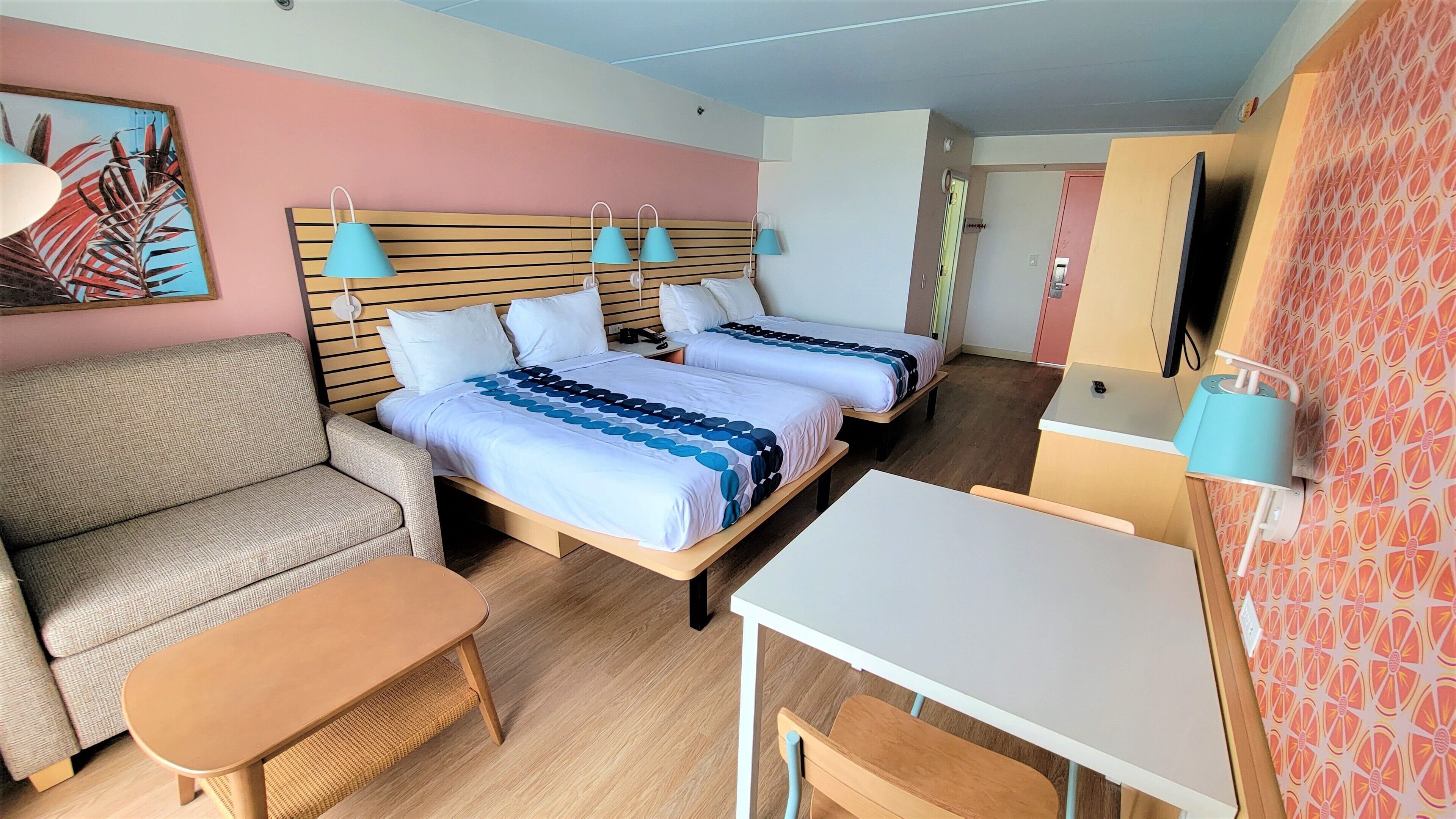 A hotel room with two beds, a sofa, a table, and a TV.