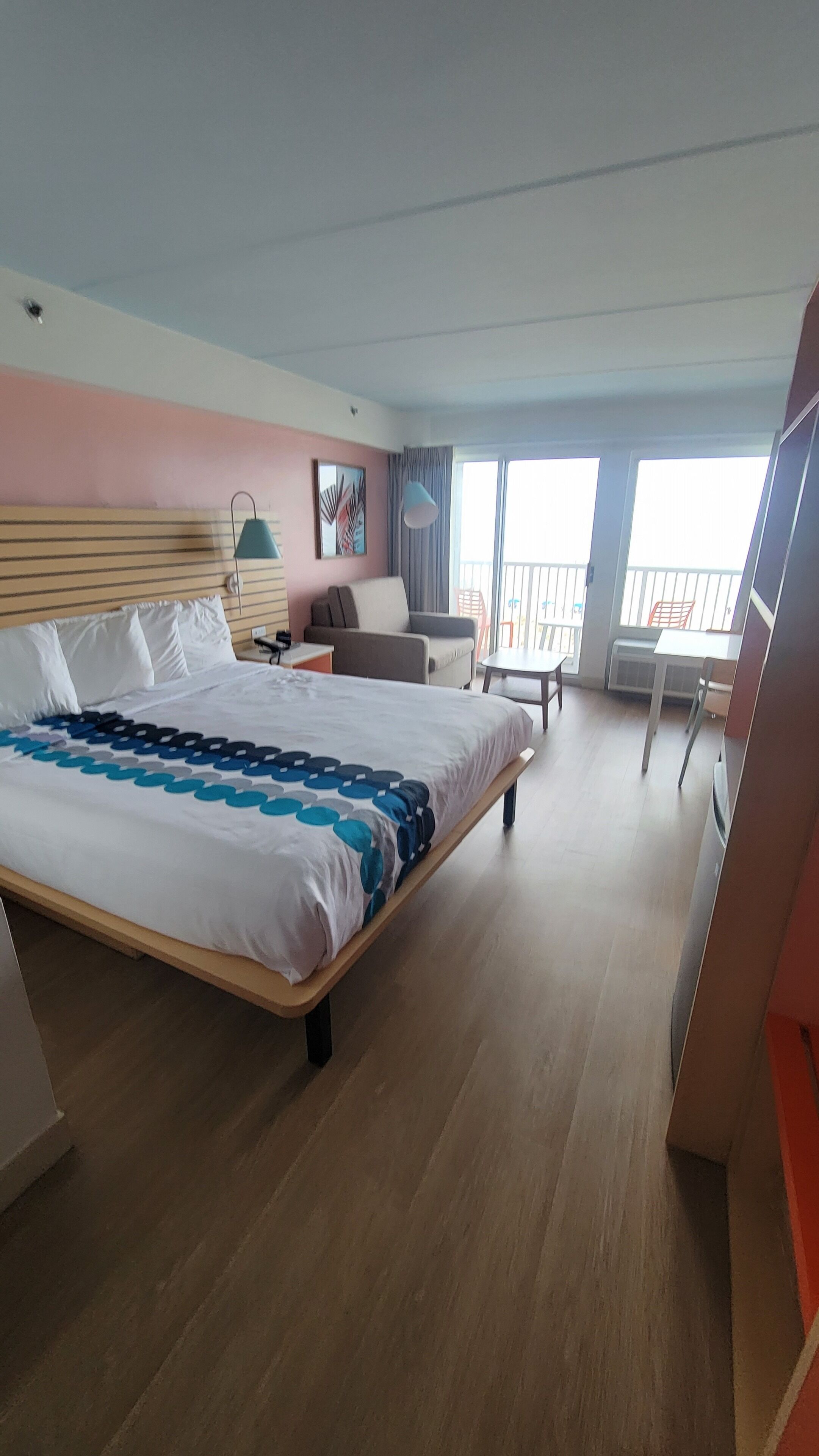 A hotel room with a large bed, a desk, a chair, a balcony, and a view of the outside.