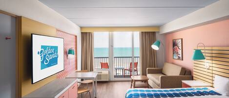 A hotel room with a bed, a desk, a chair, a sofa, a TV, and a view of the ocean.