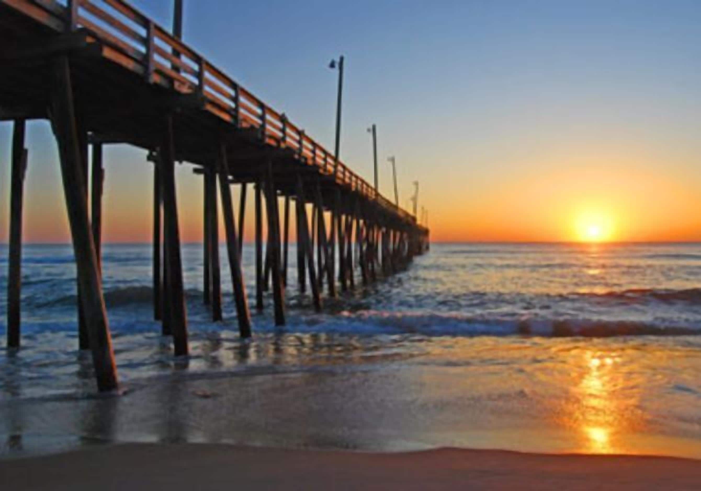 Un muelle que se adentra en el agua, con un atardecer al fondo.