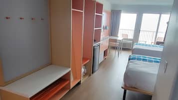 Quarto com cama, escrivaninha, guarda-roupa e uma pequena cozinha.