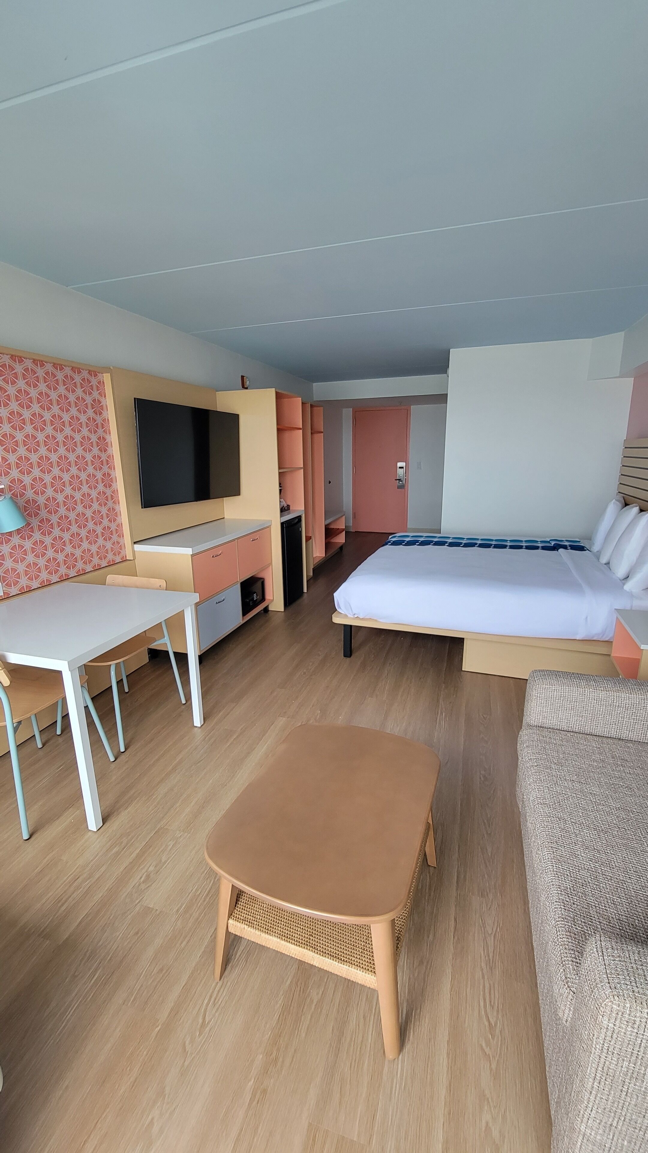 A compact hotel room with a bed, a desk, a TV, and a small seating area.