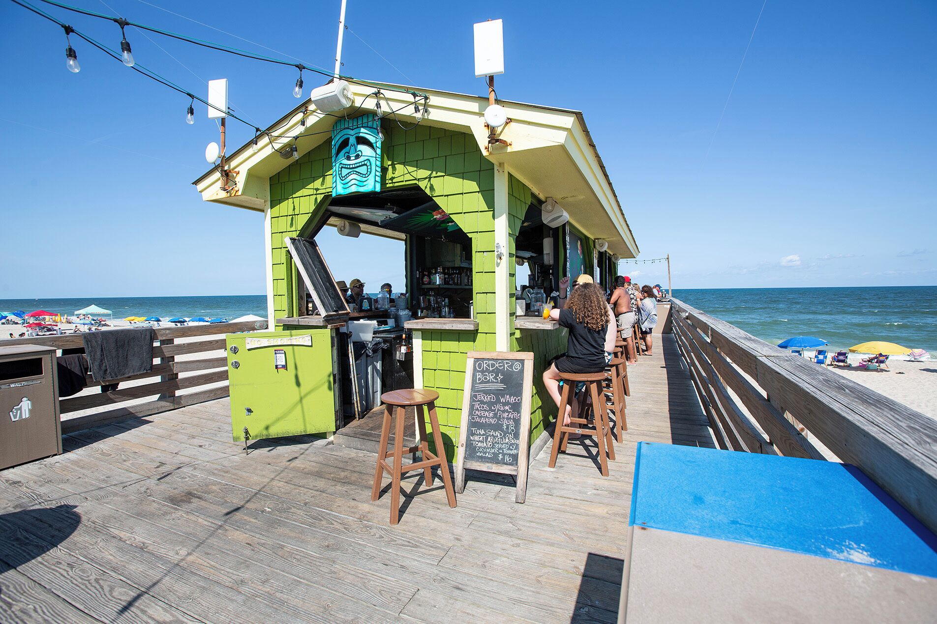 A beachside bar with a green exterior, wooden deck, and a chalkboard menu.