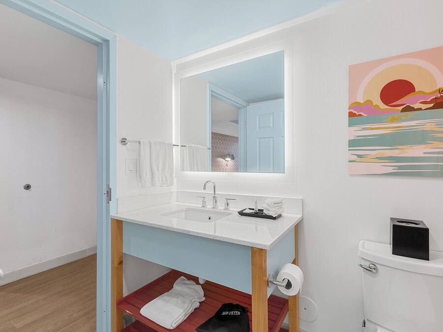 Een badkamer met een witte wastafel, spiegel en toilet. Handdoekrek met handdoeken, een klein plankje en een toiletrolhouder.