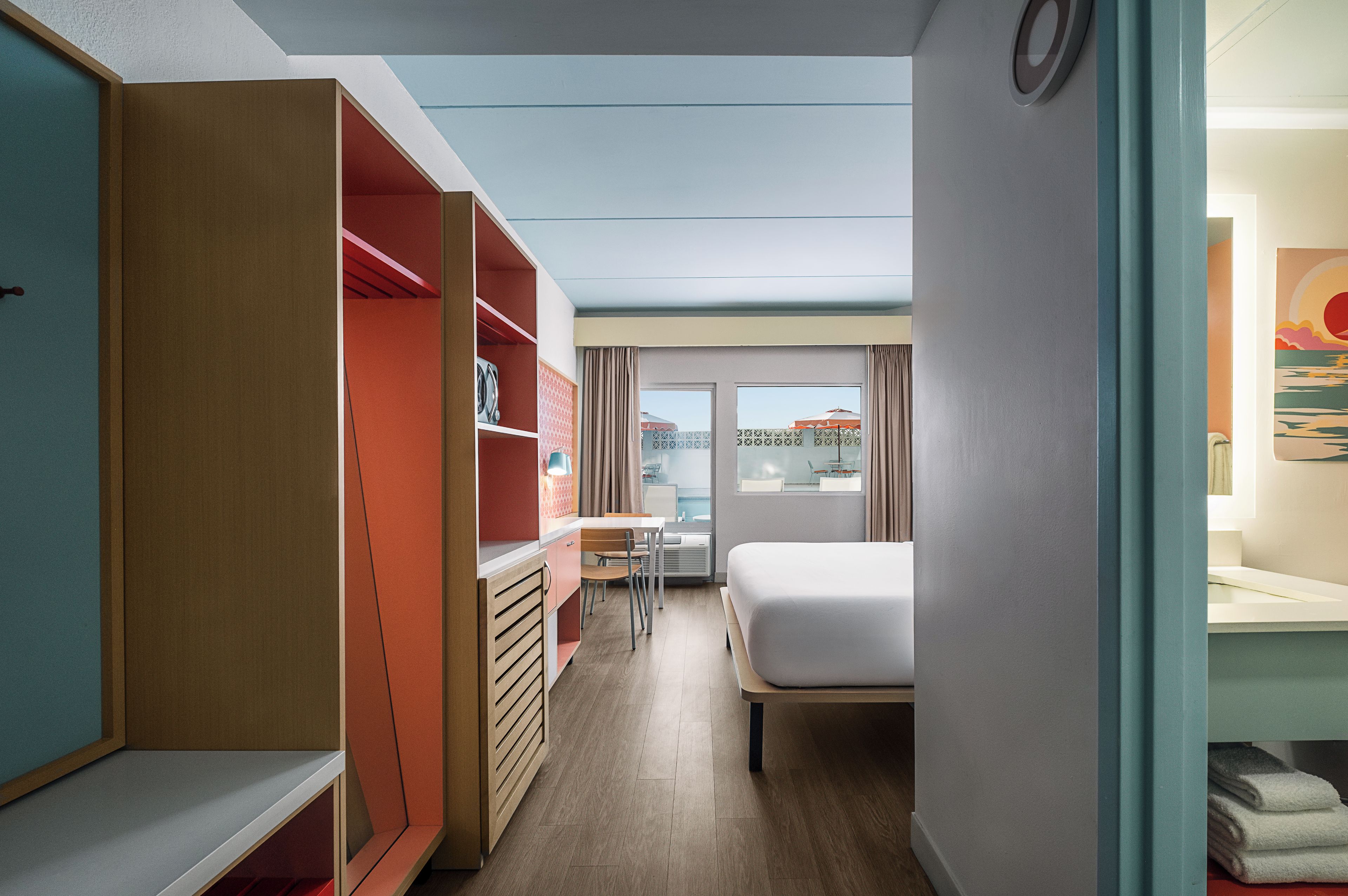 Habitación de hotel con cama, escritorio y armario. Se ve una ventana con vistas al exterior.