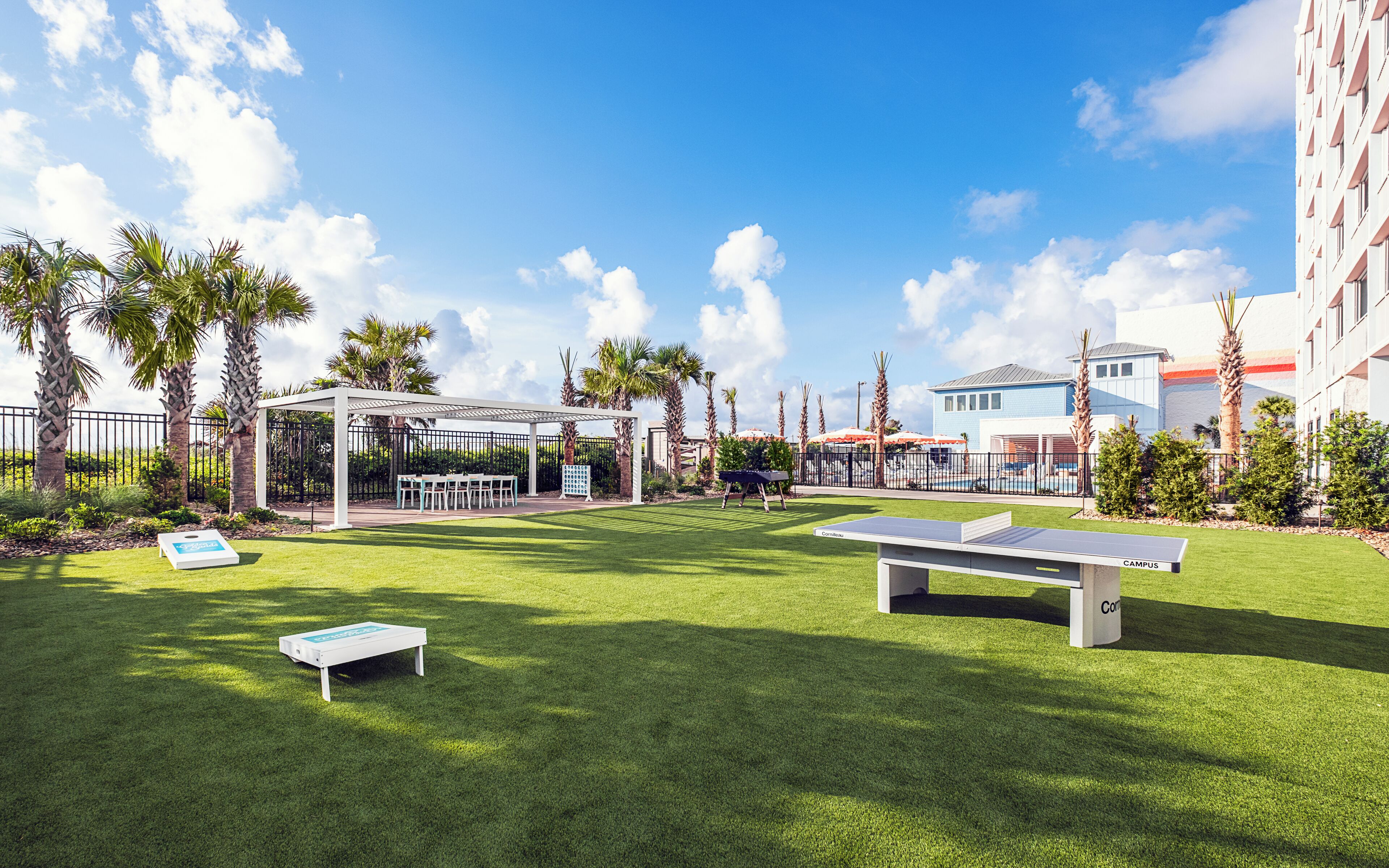A well-maintained outdoor area with a ping pong table, a covered seating area, and a pool in the background.
