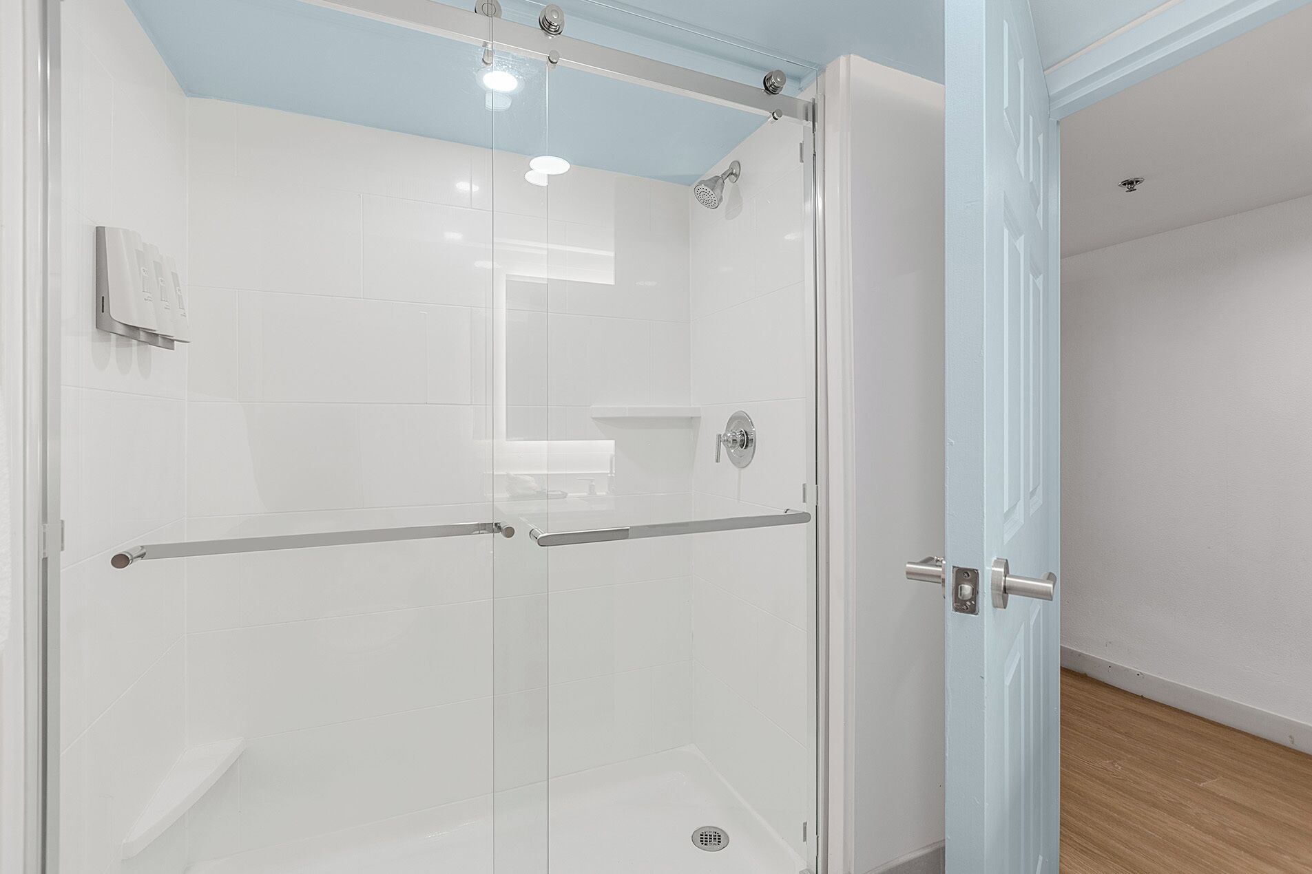 Een douche met glazen wanden, een wit betegeld interieur, een metalen handgreep en een klein plankje.