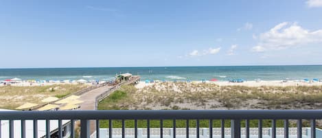 A beach view with a wooden deck, lounge chairs, and a pool.