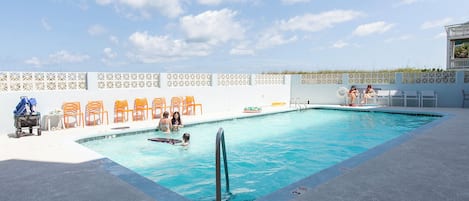Una piscina con cerca blanca, sillas de descanso y una silla para salvavidas.