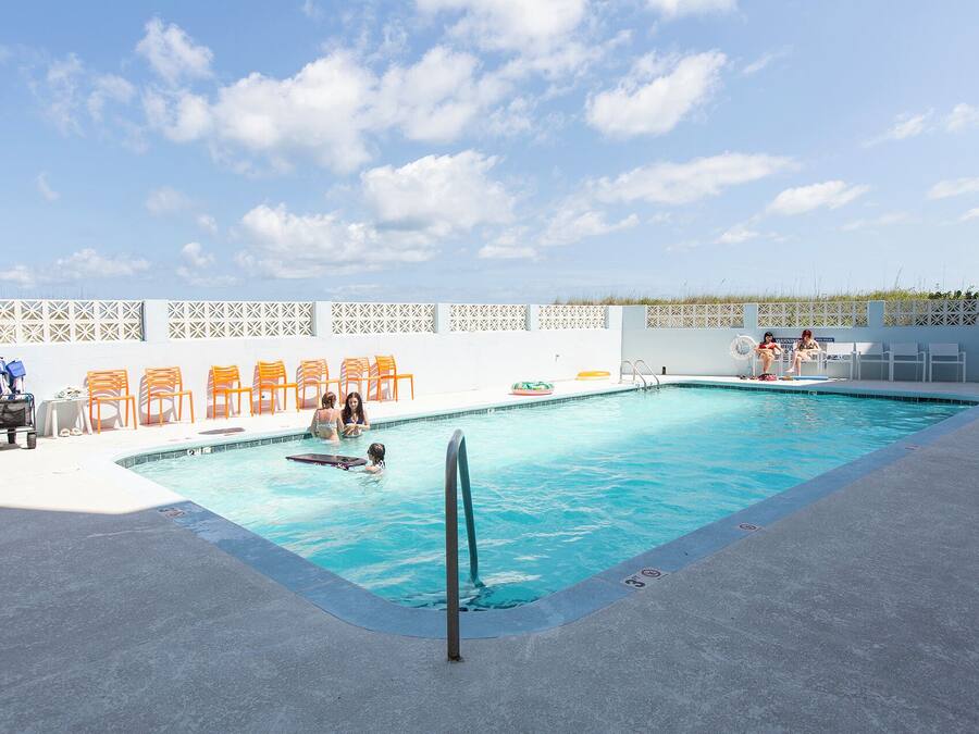 Una piscina con cerca blanca, sillas de descanso y una silla para salvavidas.