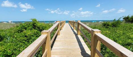 A wooden boardwalk leading to a beach with lush greenery on both sides.