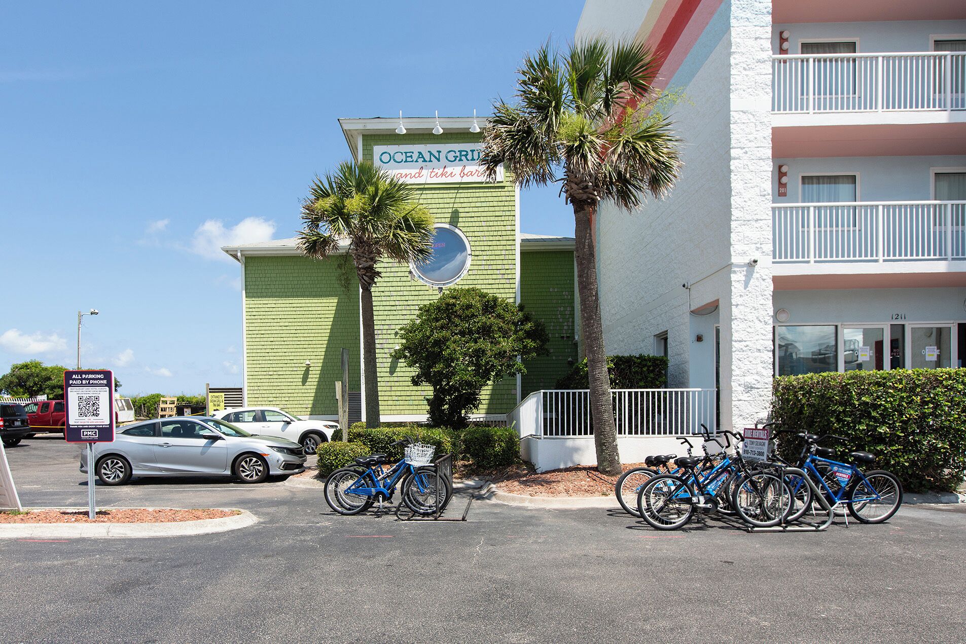 A building with a sign for 'Ocean Grid' and 'time bar'. There are bicycles parked in front and a car in the parking lot.