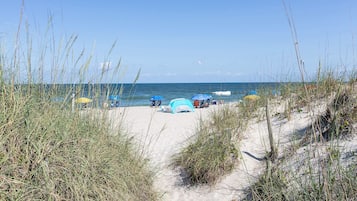 A beach with tents and umbrellas, sandy paths, and tall grasses.
