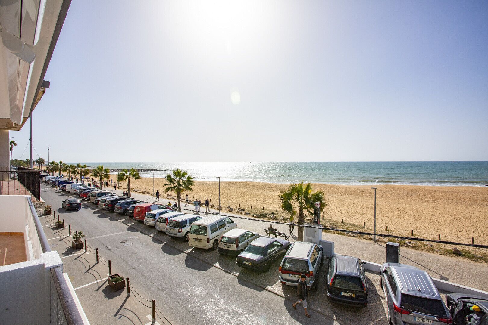 A parking lot with cars and a beach in the background.