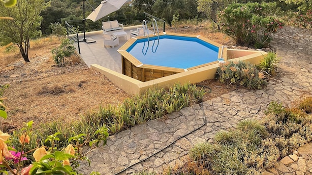 A hot tub with a wooden deck, surrounded by plants and a view of a valley. - Casa do Castelao (Loulé)