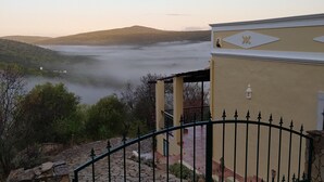 A view of a mountainous landscape with a body of water and mist. There is a building with a balcony and a fence in the foreground. - Casa do Castelao (Loulé)