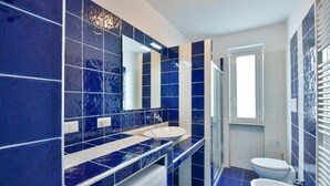 Een moderne badkamer met blauwe tegels, een dubbele wastafel, een toilet en een douchehoek.