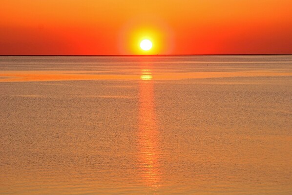 Een zonsondergang boven een rustige zee met een heldere horizon.