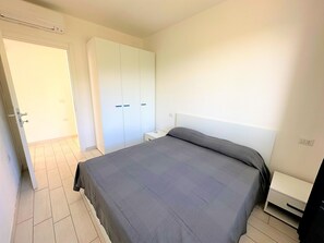 Een slaapkamer met een bed, een kledingkast, een nachtkastje en een verwarming.