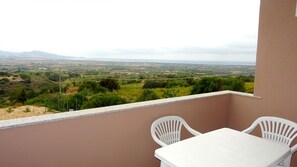 Een balkon met een tafel en twee stoelen, met uitzicht op een landelijk landschap met velden en verre bergen.