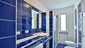 Um banheiro moderno com azulejos azuis, uma pia dupla, vaso sanitário e área de chuveiro.