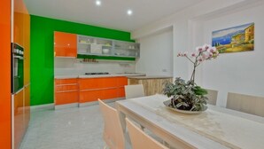 Uma cozinha moderna com armários verdes e laranja, uma área de refeições com mesa e cadeiras, e um quadro na parede.