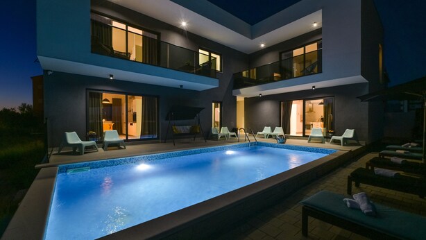 A modern two-story house with a swimming pool, outdoor seating, and a well-lit interior. - Villa Vistamar with private heated pool for 16 (Novalja)