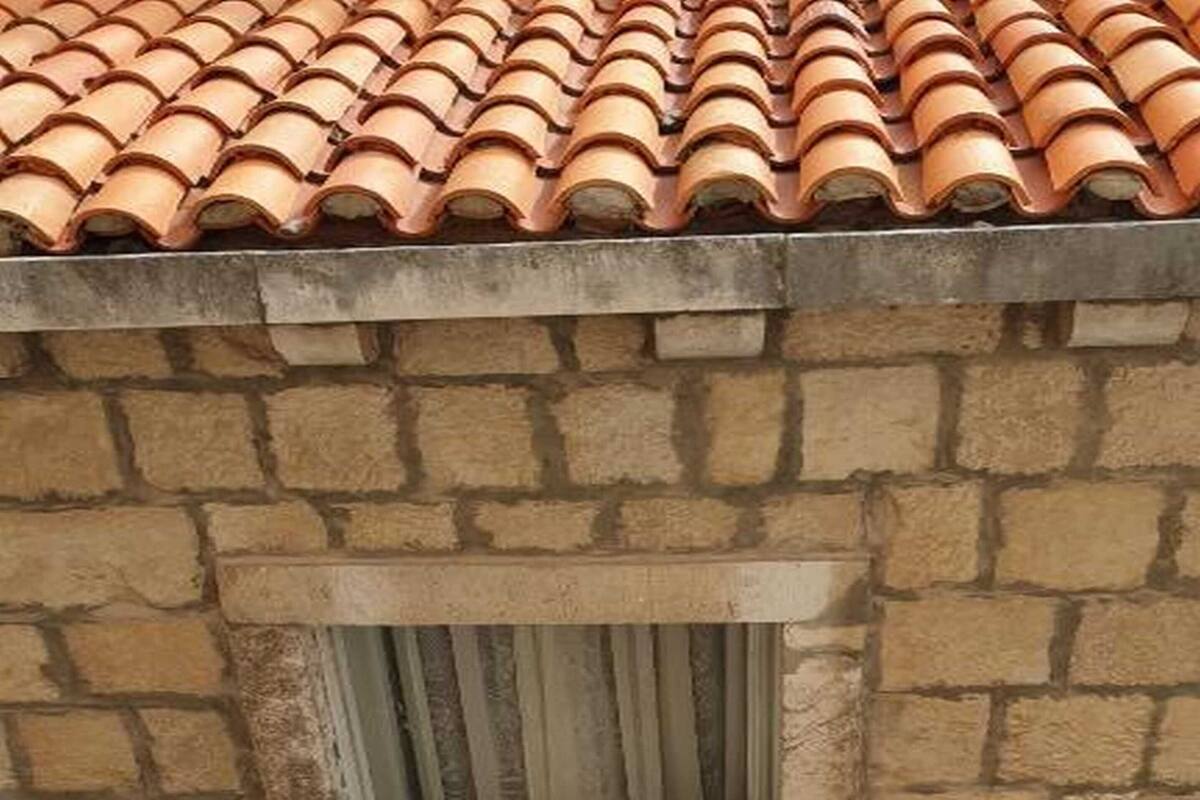 Une fenêtre donnant sur un mur de pierre et un toit recouvert de tuiles.