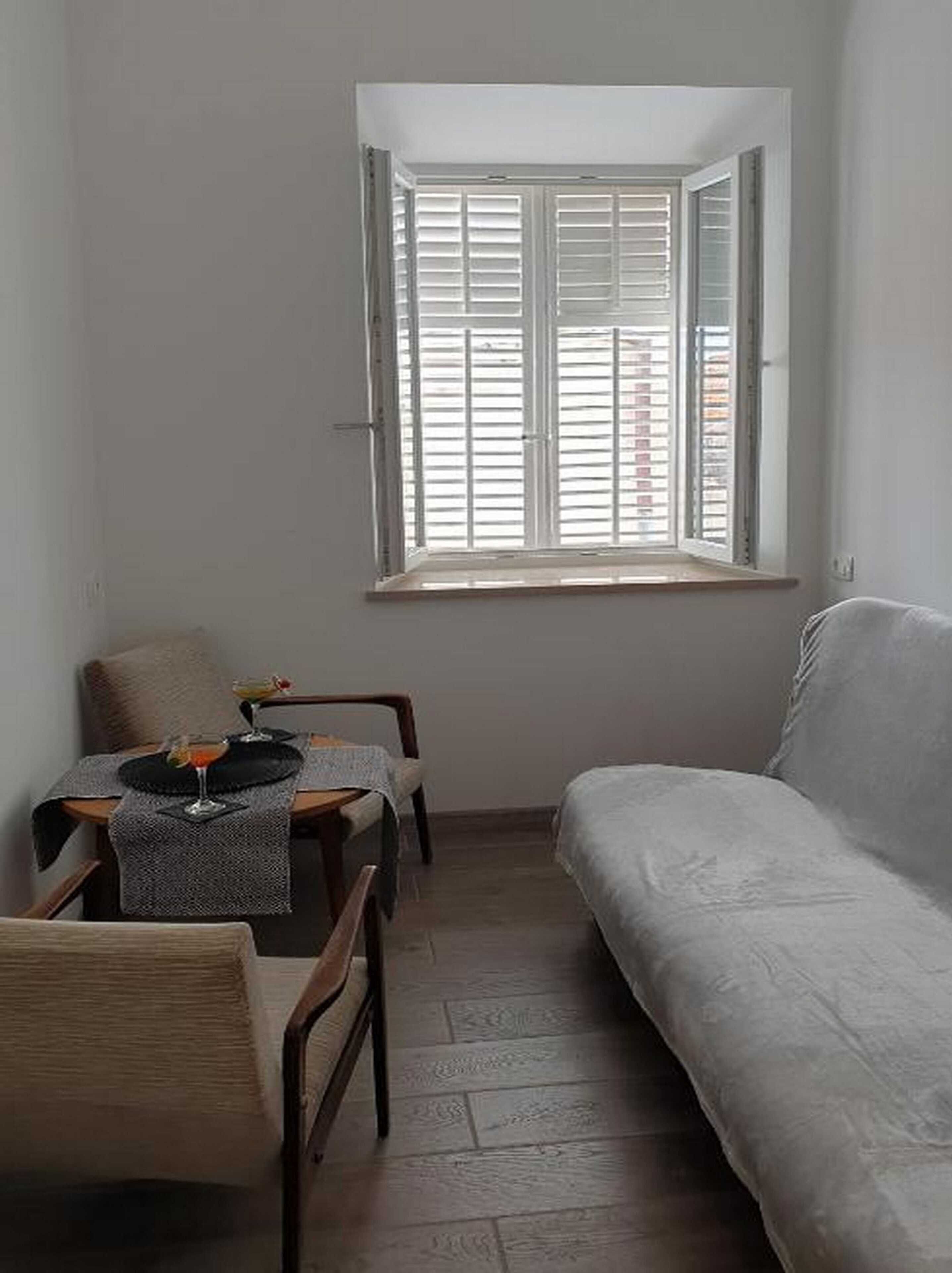 Een knus, klein kamertje met een enkel raam, een bank en een tafel met twee stoelen.