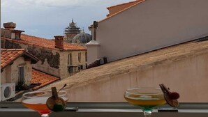 A balcony with two cocktails on black coasters, overlooking a cityscape with traditional buildings and a dome structure. - PK Apartments - Dubrovnik (Dubrovnik)