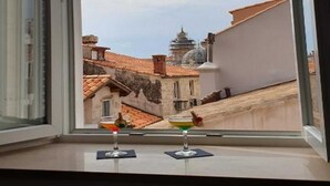 A window with a view of a cityscape, including buildings with red-tiled roofs and a dome structure. - PK Apartments - Dubrovnik (Dubrovnik)