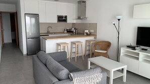 A modern kitchen with a built-in oven, microwave, and sink. There is a grey sofa and a small white table in the living area. - frontline 2 bedroom apartment (Tías)
