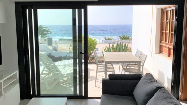 A room with a sliding glass door leading to an outdoor seating area with a view of the ocean. - frontline 2 bedroom apartment (Tías)