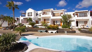 A modern resort with a swimming pool, white buildings, and tropical landscaping. - frontline 2 bedroom apartment (Tías)