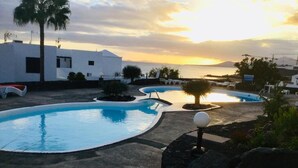 A resort pool area with multiple swimming pools, palm trees, and a sunset view. - frontline 2 bedroom apartment (Tías)