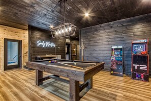 A pool table in a room with wooden walls and a neon sign.