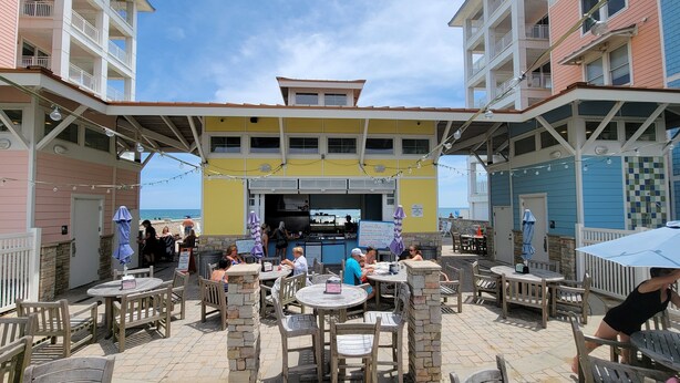 Un patio al aire libre con mesas, sillas, una barra y vista a la playa.