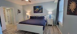 A bedroom with a bed, two bedside tables, a ceiling fan, and artwork on the walls. - Sandbridge 3bd with stunning Bay views!  Beach front complex! Newly remodeled! (Virginia Beach)