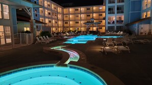 Un patio de hotel con piscina, sillas de descanso y un edificio de varios pisos con balcones.