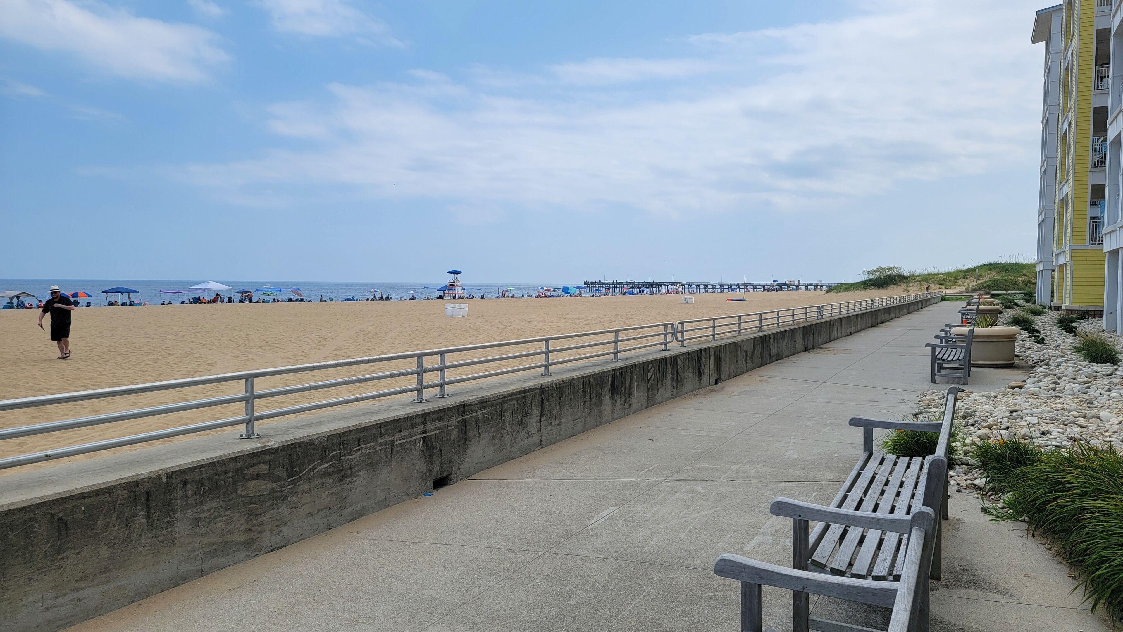 A beachside promenade with a concrete walkway, benches, and a railing.