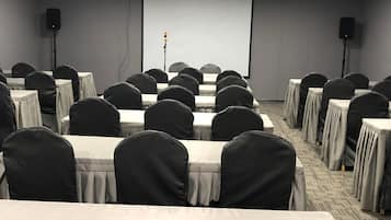 A conference room with rows of tables and chairs, a projector screen, and speakers.