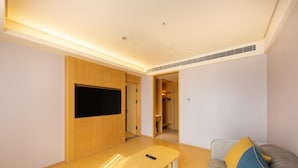 A modern living room with a flat-screen TV, a wooden table, a sofa with colorful cushions, and a walk-in closet.