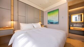A modern hotel room with a large bed, a bedside table, a nightstand, a wall-mounted painting, and a bathroom with a mirror and sink.