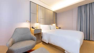 A modern hotel room with a large bed, a grey armchair, bedside tables, and a built-in wardrobe.