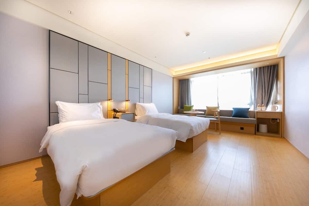 A hotel room with two beds, a sofa, a small table, and a window with curtains.