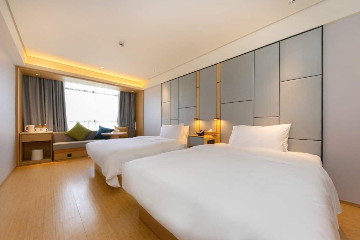 A hotel room with two beds, a sofa, a small table, and a window with curtains.
